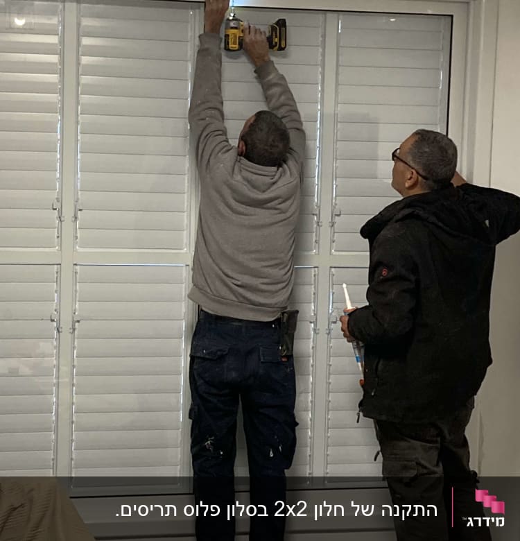 שני אנשים מתקינים תריסי אלומיניום עם מקדחה